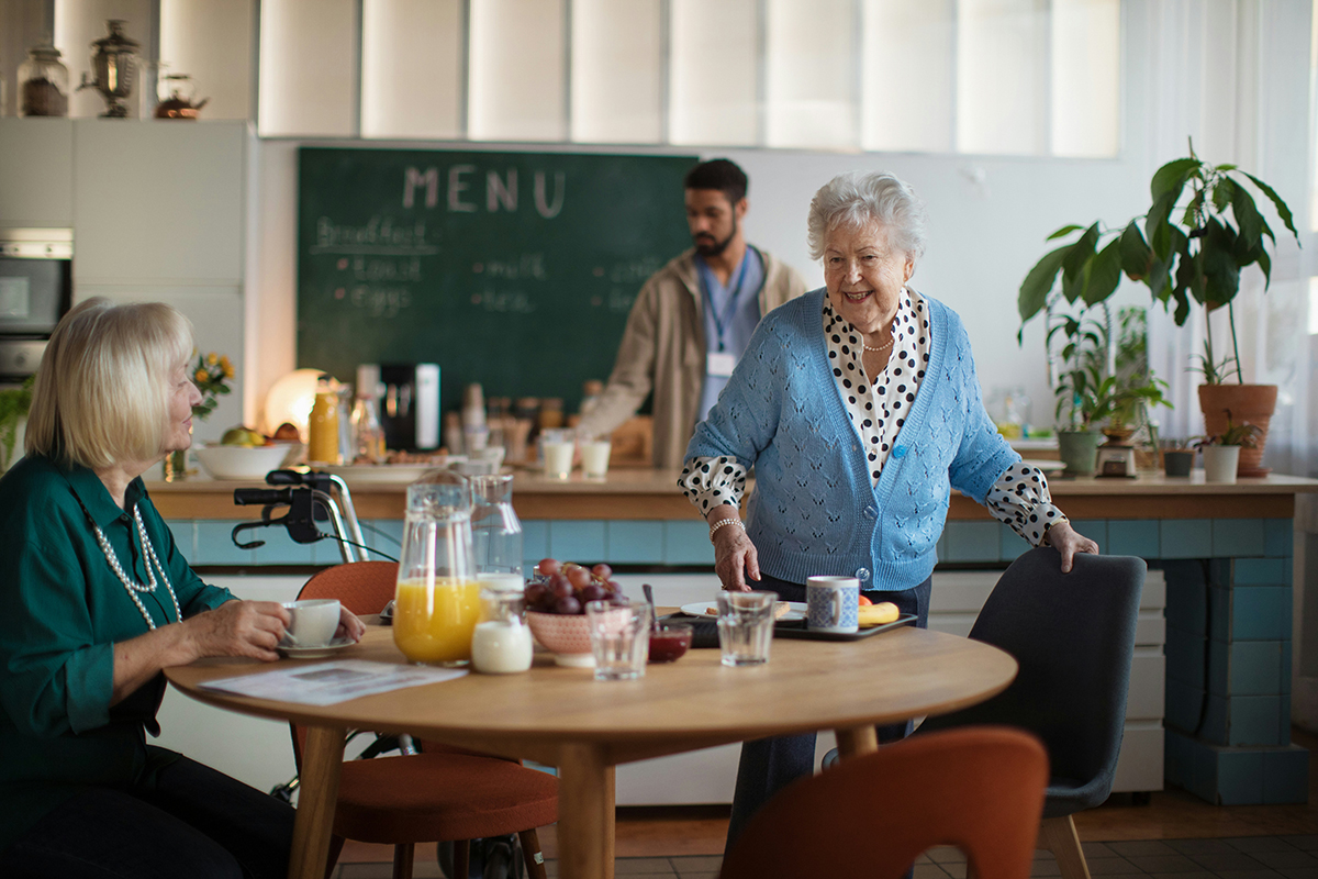 Two older ladies at a table in a cafe setting, with food and drink items on the table