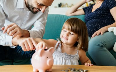 Man and woman sat on sofa with little girl putting money in piggy bank