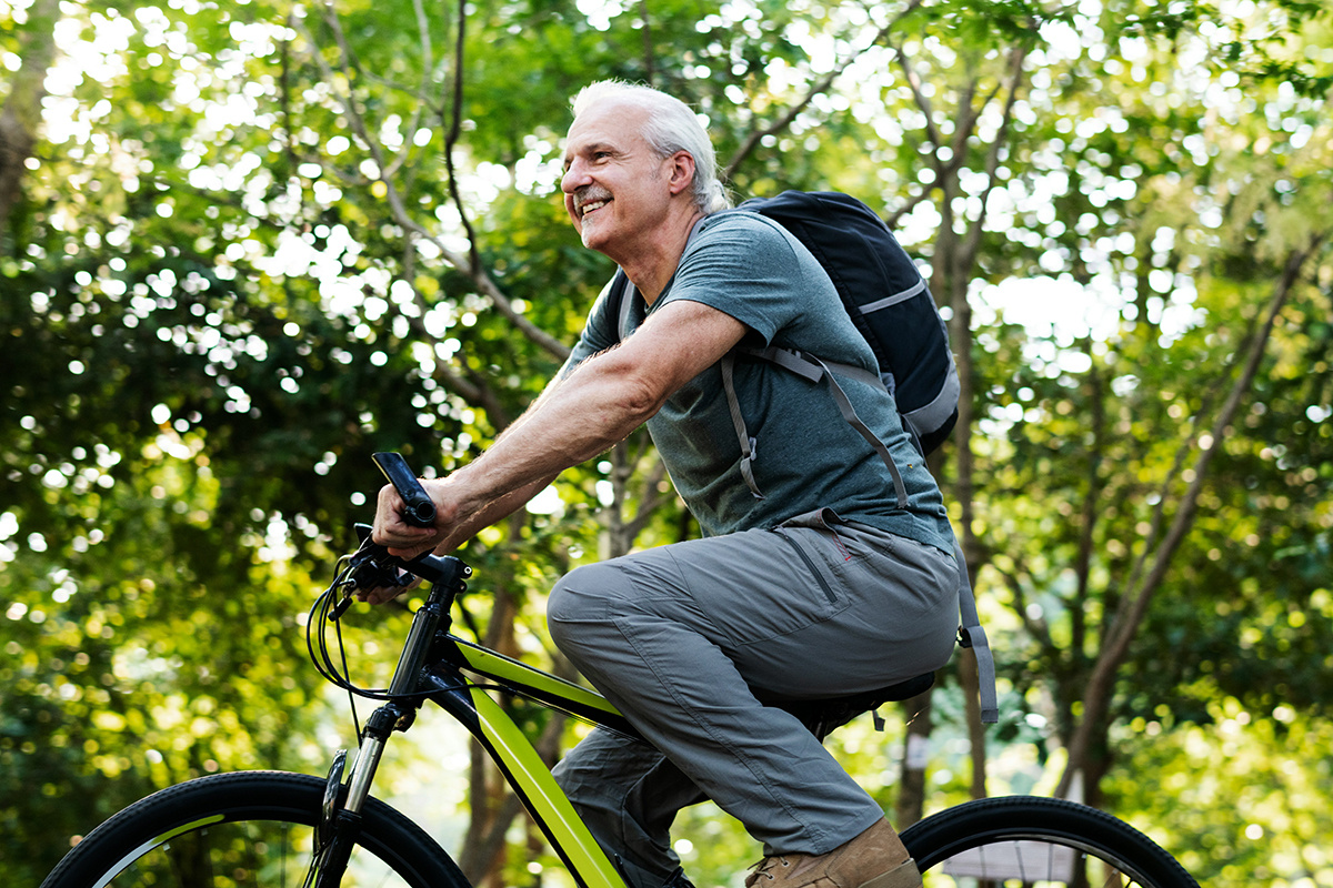 Man on bike cycling left with a background of trees