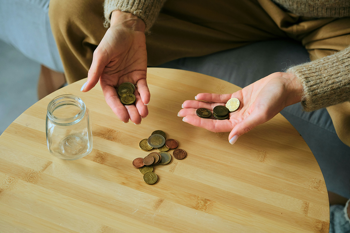 Person sat at table with empty jar and coins on low table and coins in open palms