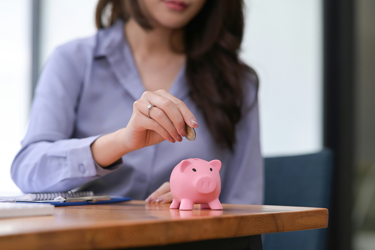 A photo of a lady holding a coin over a piggy bank on a table